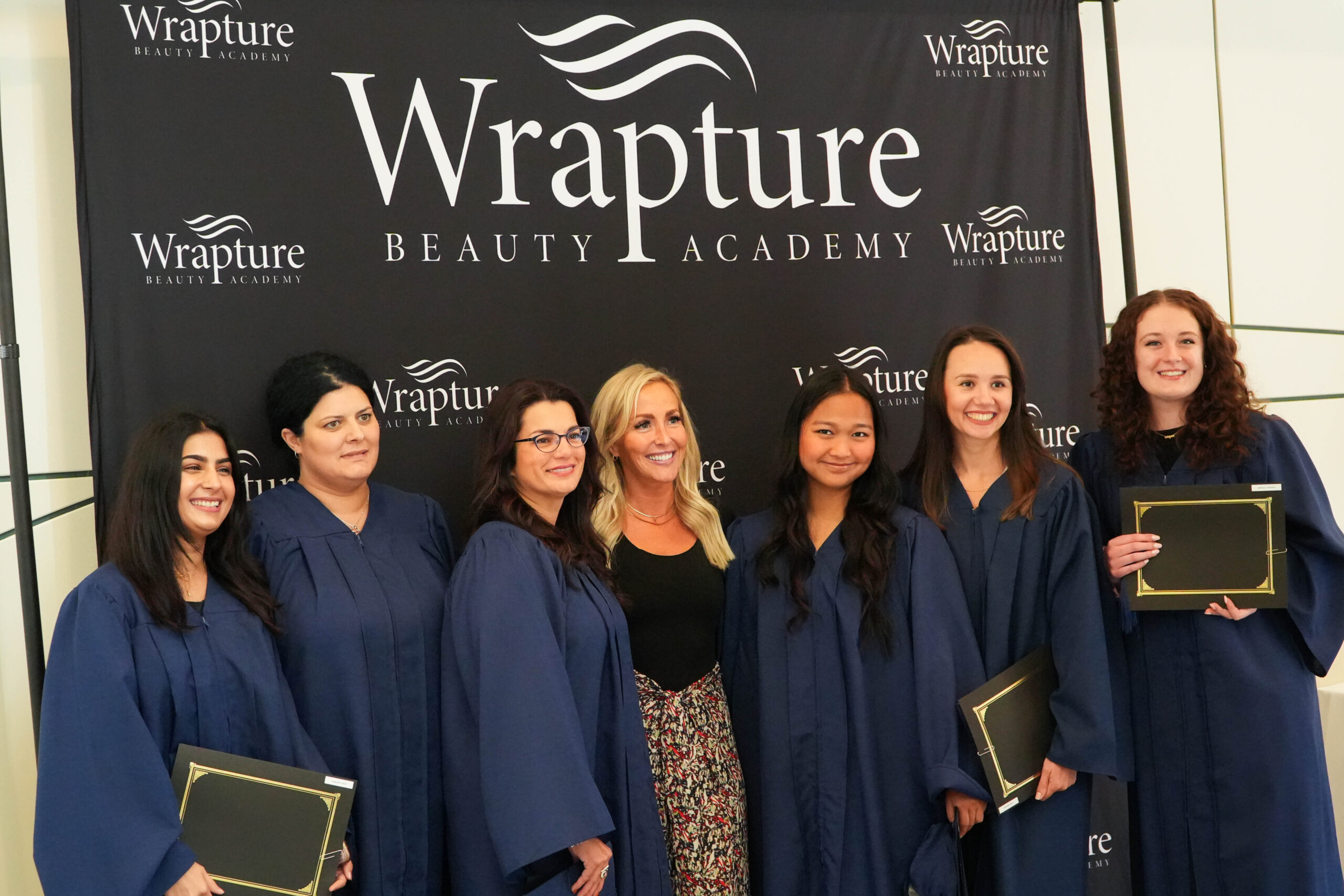 Wrapture Beauty Academy graduates smiling proudly with their faculty after the graduation ceremony in Winnipeg