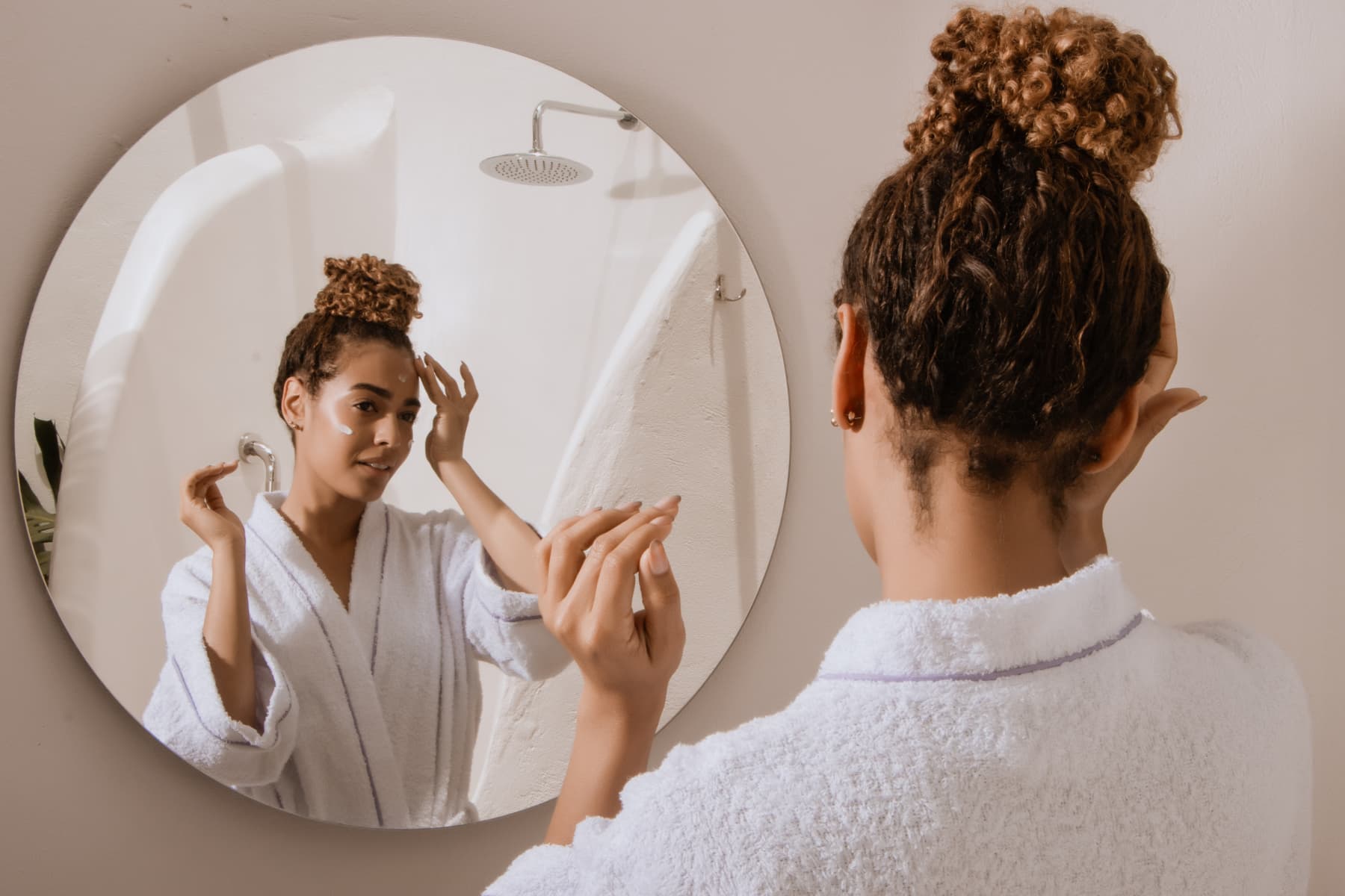 Woman in a robe applying eye cream in front of the mirror, focusing on skincare ingredients that support hydration and brightness.