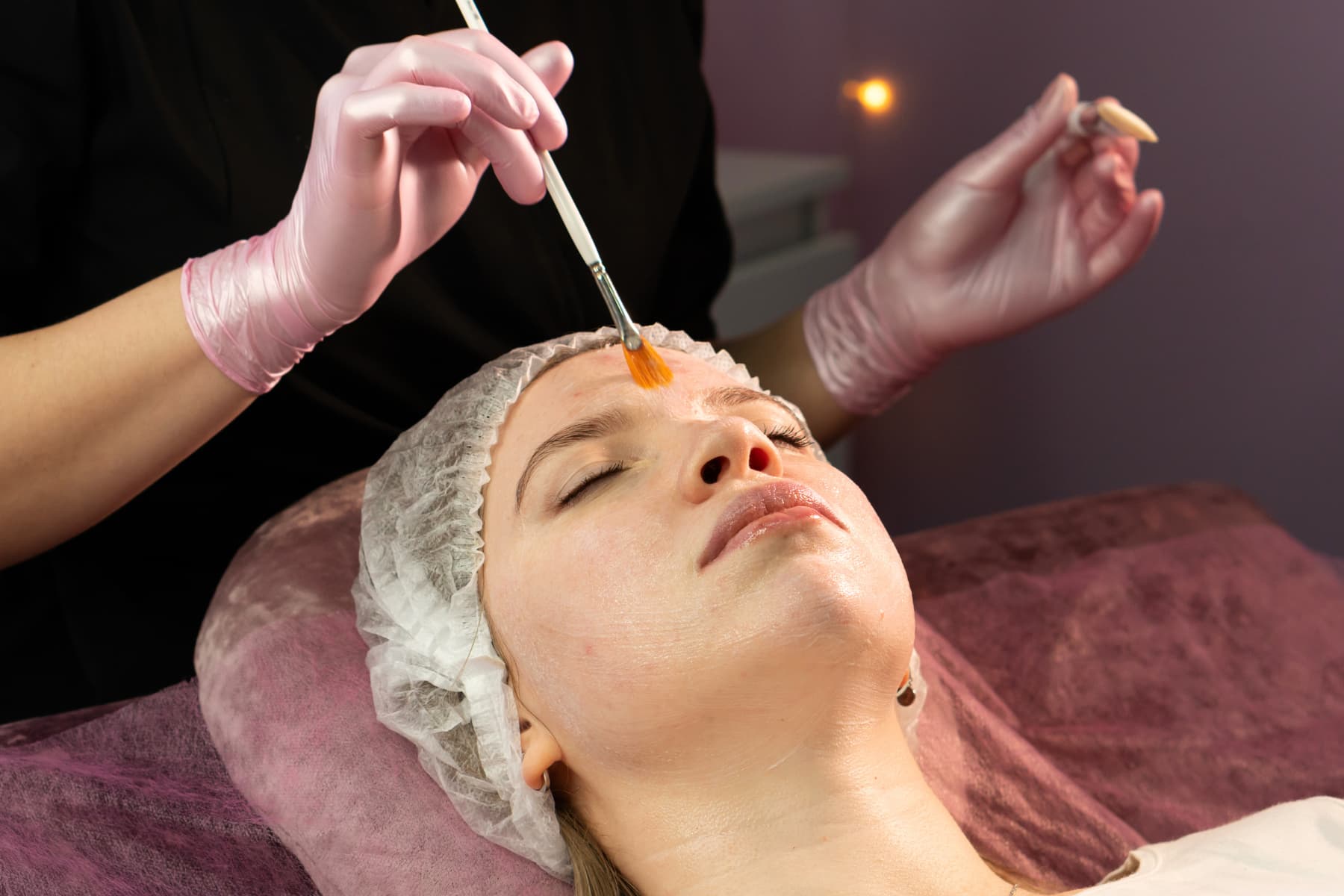 Esthetician applying a chemical peel with a brush, a treatment that relies on active skincare ingredients like AHAs to brighten and smooth the skin. facial